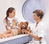 A technologist sits with a child before a CT scan